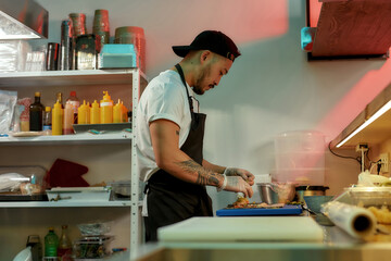 Side view of professional sushi chef looking focused while adding ingredients, spreading them over nori sheet, making delicious rolls at commercial kitchen