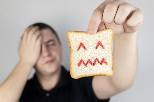 Conceptually about gluten intolerance. The man holds in his hand a piece of bread on which an angry expression is painted. Celiac disease, fear of cereals, manifestation of allergies
