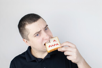 Conceptually about gluten intolerance. The man holds in his hand a piece of bread on which an angry expression is painted. Celiac disease, fear of cereals, manifestation of allergies