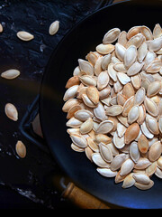 Roasted pumpkin seeds in a black plate on a dark background