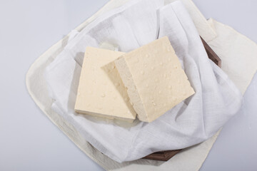 a block of two tofu in the cotton on the wood tray.