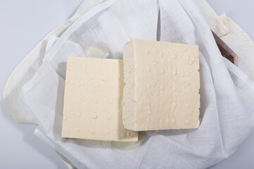a block of two tofu in the cotton on the wood tray.