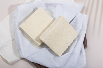 a block of two tofu in the cotton on the wood tray.