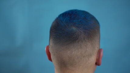 A young man is dyed his hair blue. A alternative people is painted with temporary hair dye from a spray can. The view from the back.