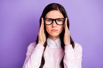 Portrait of attractive focused tense wavy-haired girl looking suspiciously touching specs isolated over violet color background