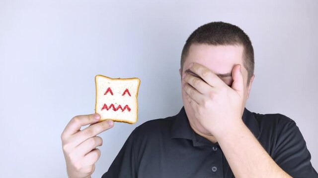 Conceptually about gluten intolerance. The man holds in his hand a piece of bread on which an angry expression is painted. Celiac disease, fear of cereals, manifestation of allergies