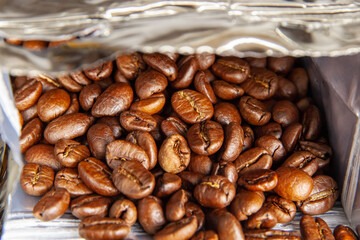 Medium-roasted coffee beans are in an open package. Close-up