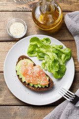 Whole grain rye bread toast with salmon and avocado on wooden table background. Flat lay, top view