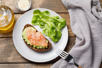 Whole grain rye bread toast with salmon and avocado on wooden table background. Flat lay, top view