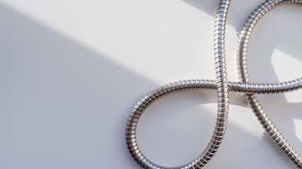 Metal shower hose on white background. Flexible chrome tube. Corrugated plumbing tube on geometrical banner with copy space on hard sunlight and shadow.