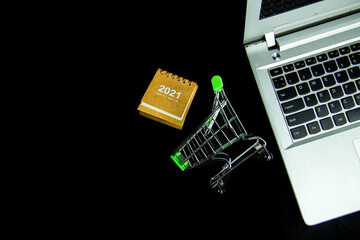Top view shopping cart and Calendar 2021 near laptop with black background. Black Friday sale online shopping, Financial and Business Shopping. Technology, Ecommerce concept. Copy space.