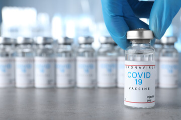 Doctor taking glass vial with COVID-19 vaccine from table, closeup. Space for text