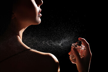 Woman spraying luxury perfume on black background, closeup - obrazy, fototapety, plakaty