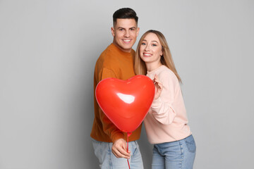 Fototapeta na wymiar Lovely couple with heart shaped balloon on grey background. Valentine's day celebration