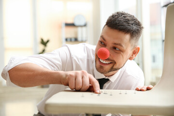 Man with clown nose putting pins on colleague's chair in office. Funny joke
