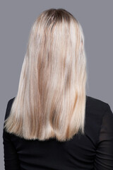 Back shot of lady with highlighted blonde hair without radiant toning and extension. Girl in black blouse is posing on the gray background. 