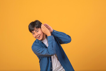 Asian man covering his ear with his hand to listen On orange background.