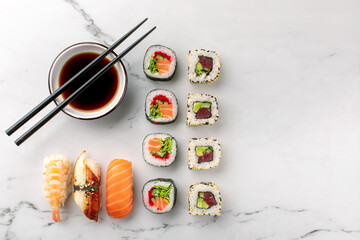 Nigiri sushi, maki rolls and soy sauce on a white stone background and chopsticks on the side. Traditional Japanese food, top view, copy space.