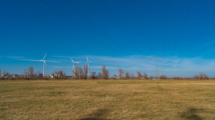Panoramic view over farm landscape with wind turbines to generate green electrical power and high power electrical line wires crossing blue sky, Magdeburg, Germany.