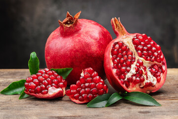 Healthy pomegranate fruit with leaves and half of ripe pomegranate on a cutting board, side view,...