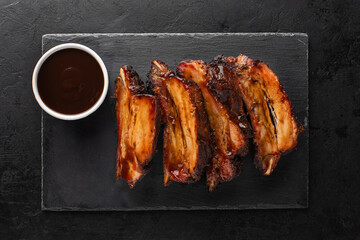 Smoked pork ribs and barbecue sauce side view on black slate board, top view.