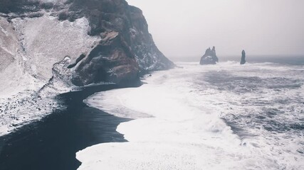 Reynisfjara black sand beach in Iceland with basalt rocks covered with snow aerial view on a stormy winter day. Unreal and spectacular travel destination. - Powered by Adobe