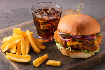 Fast food set. Yummy chicken burger with cheese, fries and a glass of cola on a wooden board on a...