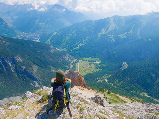 Fototapeta na wymiar Woman with backpack resting on mountain top, looking at view dramatic landscape valley summer activity fitness wellbeing freedom concept, selective focus rear view