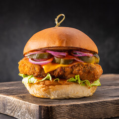 Chicken burger with cheese and pickles on a wooden board on a dark background.