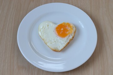 Heart shaped fried eggs on a white plate on wooden table