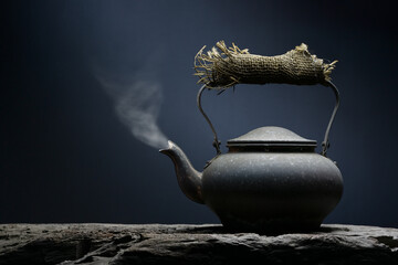 Black metal tea or coffee kettle close-up with hot steam coming out the spout still life fine art. - 417628412