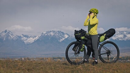 Fototapeta premium The woman travel on mixed terrain cycle touring with bikepacking. The traveler journey with bicycle bags. Sport tourism bikepacking, bike, sportswear in green black colors. Mountain snow capped.