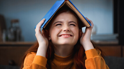 Happy teenager holding book above head at home