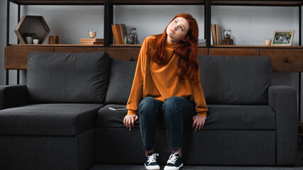 Obraz premium Pensive teen girl sitting on couch near smartphone