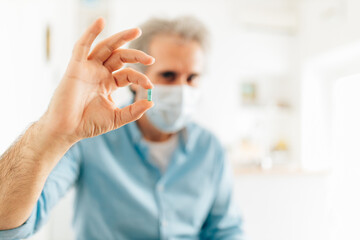 Close up of senior man with protective face mask holding a pill. Healthcare and medicine