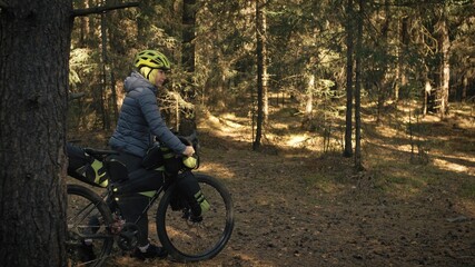 The woman travel on mixed terrain cycle touring with bike bikepacking outdoor. The traveler journey with bicycle bags. Stylish bikepacking, bike, sportswear in green black colors. Magic forest park.