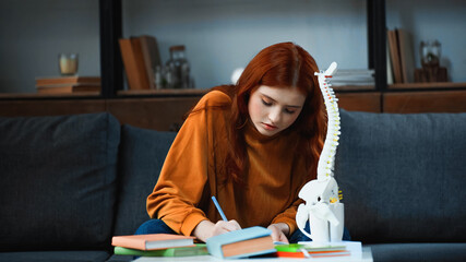 Young student holding pen near books and spinal mockup
