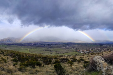Spectacular full rainbow in the mountains of Madrid, sky with dark rain clouds.