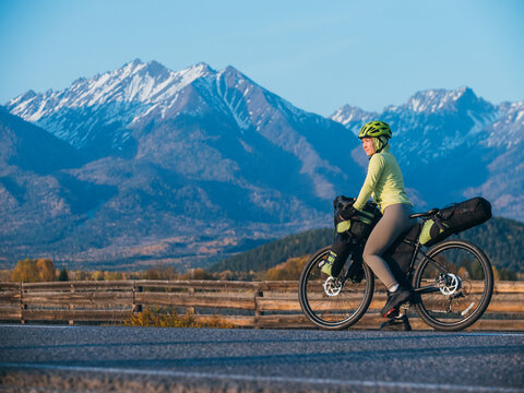 The woman travel on mixed terrain cycle touring with bikepacking. The traveler journey with bicycle bags. Sport tourism bikepacking, bike, sportswear in green black colors. Mountain snow capped.