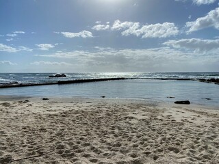 Empty tidal pool on a summer morning, clouds in the sky and the sun shining on the ocean