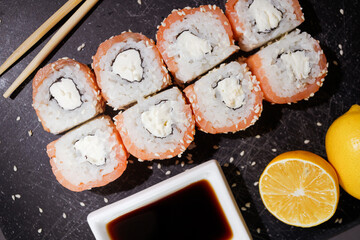 Sushi rolls set served with lemon and souce on black board on dark background. Flat layout on black, top view