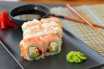 Sushi roll covered with shrimp meat on black ceramic plate