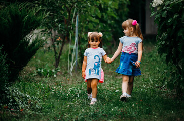 Two sisters are walking along the road to the park on a sunny summer day. Family time. Cute happy kids.