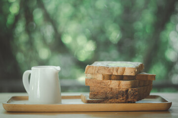 Pile of sliced chocolate bread and hot milk on wood tray.