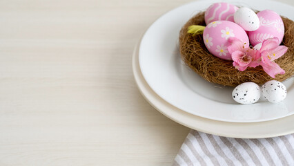 Fototapeta na wymiar Easter lunch. Holiday table. Festive catering. Invitation card. Pink white color painted eggs with modern minimal design Spring flowers in nest served in plate on light copy space.