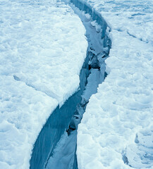Fototapeta premium Large clean crack in sea ice with white snow on the top and clear blue ice beneath. Close up.