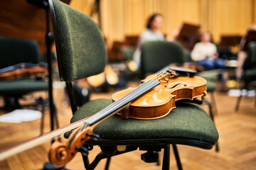 A close-up of a wooden violin, lying on a chair. The rehearsal room in the background.