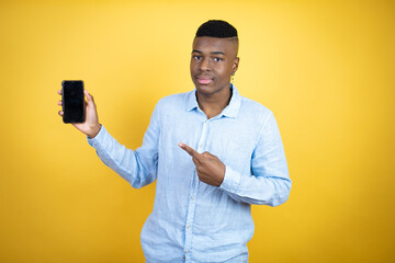 Young african american man wearing a casual shirt standing over yellow background showing screen smiling happy pointing with hand and finger