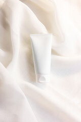 white cosmetic tube for face cream, cleanser, body lotion or shampoo on white draped cloth. Gentle...