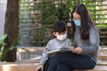 Obraz premium Asian boy with face mask reading the book with his mother